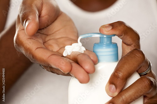 Young african-american guy squeezing a body cream from a pump on white background