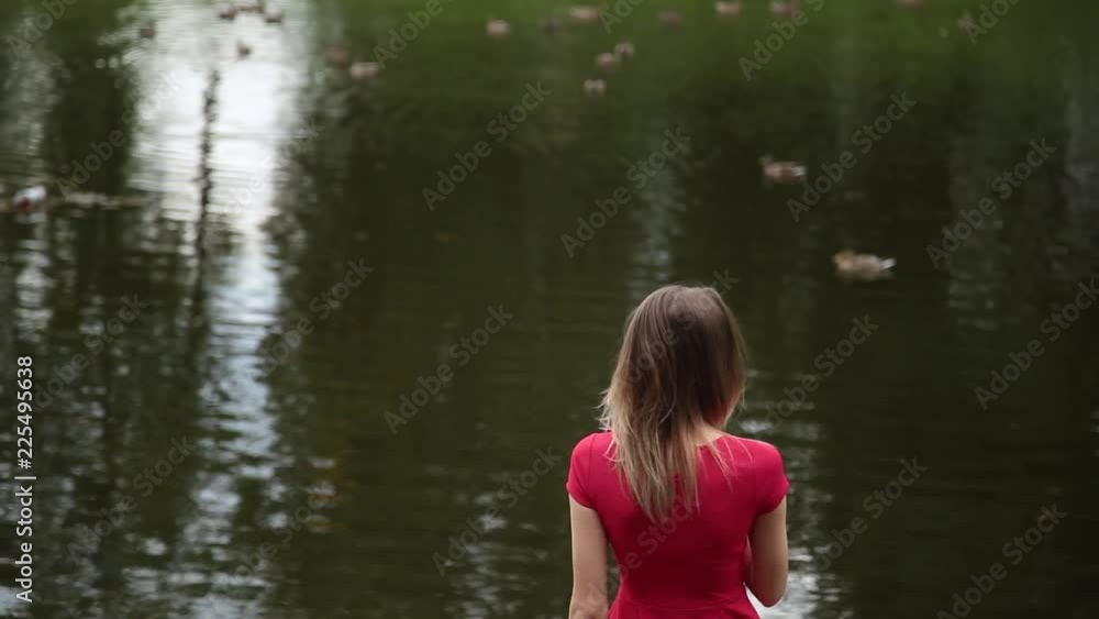 A very beautiful girl in a red dress is standing on a pier near a small lake. A very beautiful girl in a red dress is standing on a pier near a small lake.