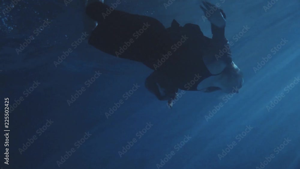 A woman in a black dress swimming in the dark pool water with some lights , trying to get out of water. A woman in a black dress swimming in the dark pool water with some lights , trying to get out of water.