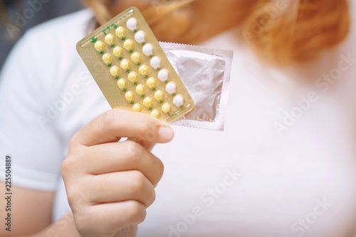Woman hands give birth control pills and condom in hand. Taking Contraceptive Pill. safe sex concept on the bed Prevent infection and Contraceptives control the birth rate or safe prophylactic.