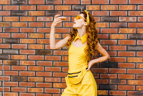 attractive young woman eating donut in front of brick wall