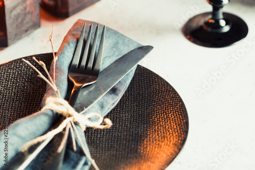 Festive table setting in a black style among black candles on a white table. Plate with fork and knife on a linen napkin. Thanksgiving or Halloween dinner. photo