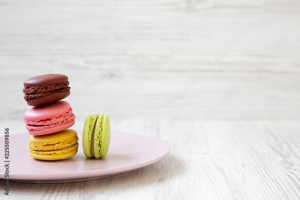 Sweet and colorful macarons on pink plate over white wooden background, side view. Close-up. Copy space. Sweet and colorful macarons on pink plate over white wooden background, side view. Close-up. Copy space.