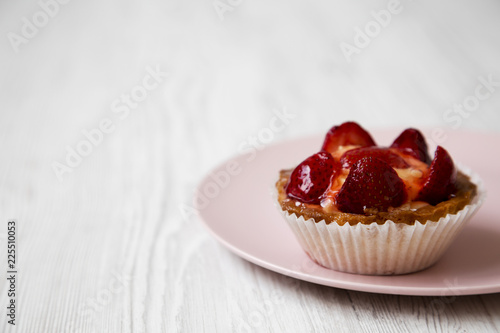 Strawberry vanilla cream cheese tart on pink plate, side view. Close-up. White wooden surface. Copy space.
