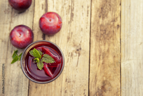 Red herbal and fruit tea in glass cup and tea with plums. Rustic textured wooden table. Copy space.