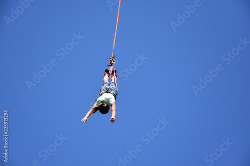 Bungee jumping from crane. Seen from the ground young woman hanging on a cord high in the blue sky