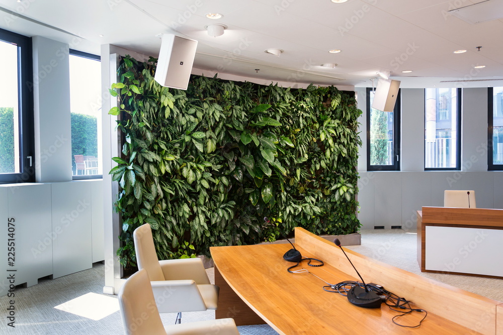 Living green wall, vertical garden indoors with flowers and plants under artificial lighting in meeting boardroom, modern office building - obrazy, fototapety, plakaty 