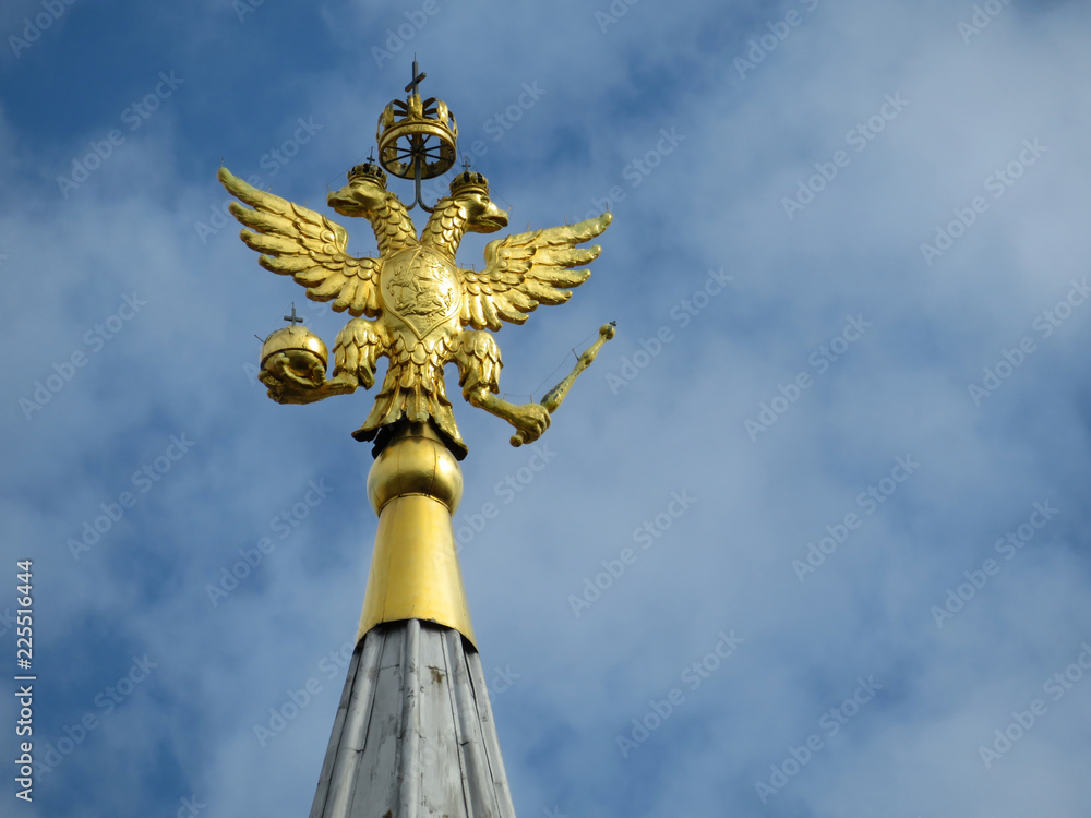 Coat of arms of Russia on blue sky with clouds. Golden Imperial eagle, Russian state emblem on top of the tower on Red square in Moscow Coat of arms of Russia on blue sky with clouds. Golden Imperial eagle, Russian state emblem on top of the tower on Red square in Moscow