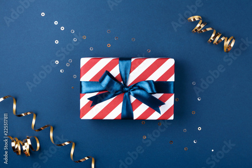 Gift box wrapped in red striped paper and tied with blue bow on blue backgrou...