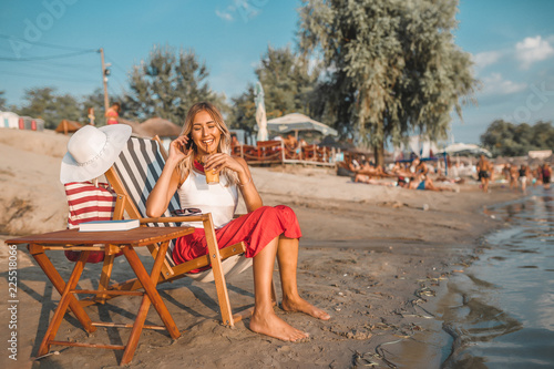 Girl talking on a phone and drinking juice on the beach