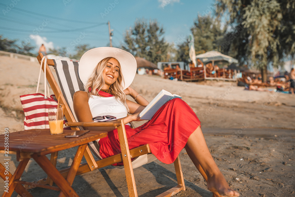 Smiling woman reading a book while sitting on deck chair