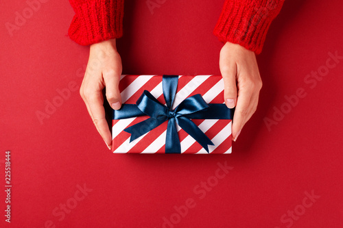 Female's hands in red pullover holding striped gift box with blue ribbon on r...