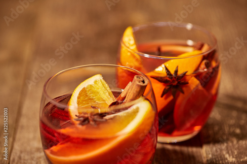 close up view of mulled wine in glasses with orange pieces and spices on wooden tabletop