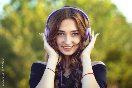 portrait of a beautiful happy teenager girl with headphones on head, young woman listening to music on the nature