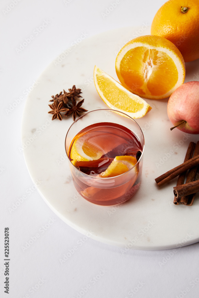 close up view of hot mulled wine in glass, spices and fresh fruits on white surface close up view of hot mulled wine in glass, spices and fresh fruits on white surface
