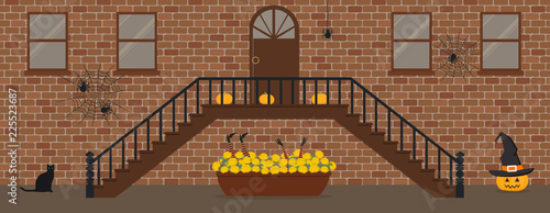 Porch, decorated for Halloween. Front Porch Halloween Decorations. There are pumpkins, spider webs and a pot of chrysanthemums and witch's feet and hands on the background of the brick facade of house