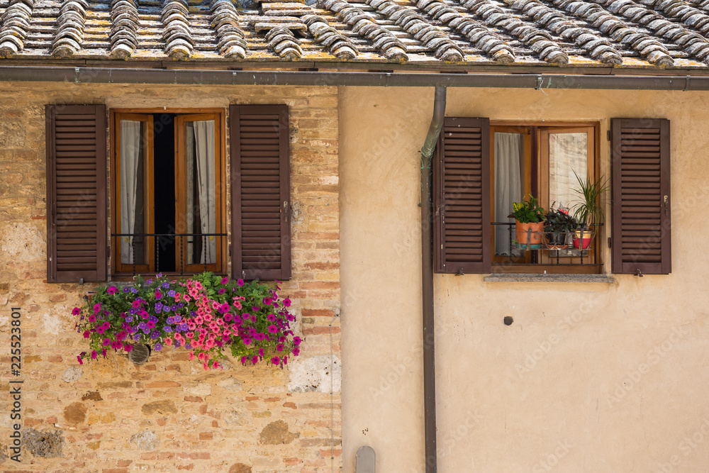 Brown shuttered window with a flowertbox of beautiful petunia flowers in San Gimignano, Tuscany, Italy