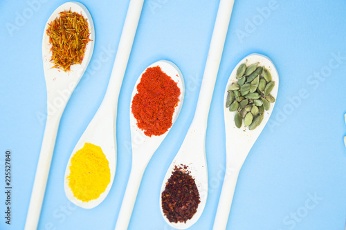 Cooking Hot Spicy Food Concept. Dry spices and herbs in wooden spoons, light blue background