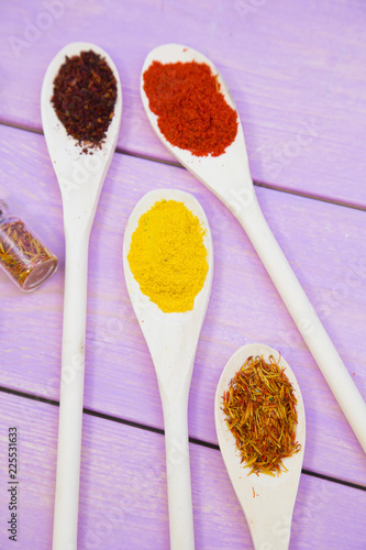 Cooking Hot Spicy Food Concept. Dry spices,beans and herbs in plastic cup, glass jar with cork and wooden spoon, purple wooden background