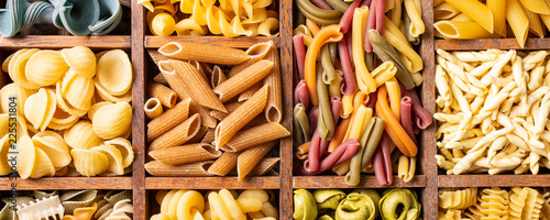 Assorted colorful italian pasta in wooden box. Healthy food background concept. Flat lay, top view. Banner. photo