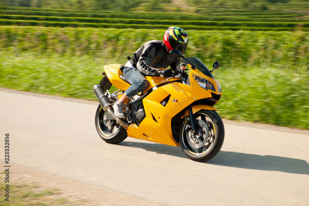 Man drive a motorbike on a country road with vineyards in background