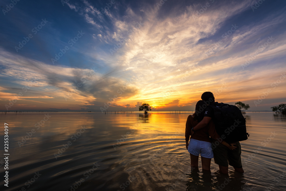 Couple in love standing in lake on sunrise with nice sky.