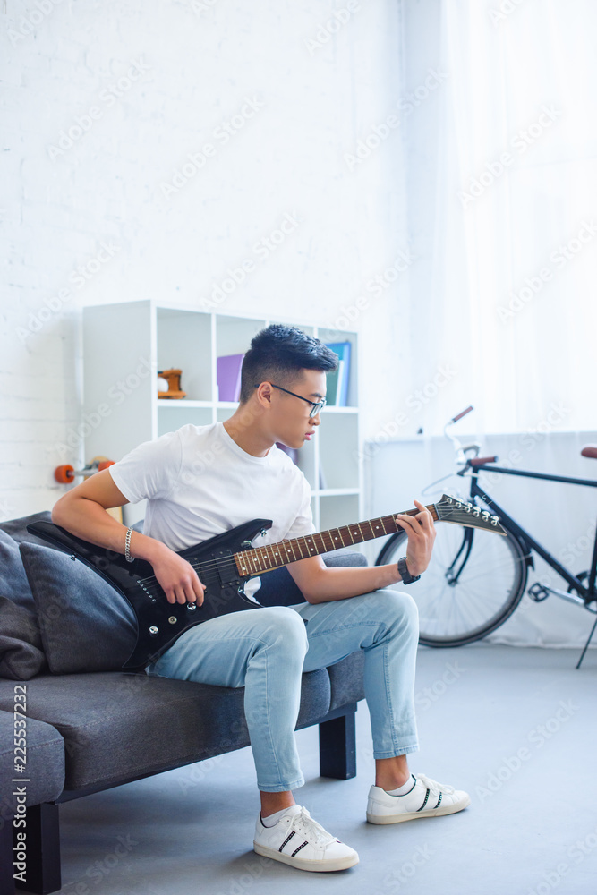 handsome asian man playing F major chord on unplugged electric guitar at home