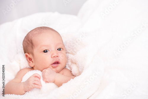 Little cute newborn girl wrapping by white fur blanket looking at camera on white bed.