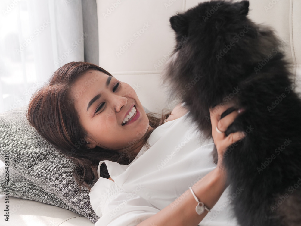 Happy Asian woman playing with her black dog on sofa at home, lifestyle concept. Happy Asian woman playing with her black dog on sofa at home, lifestyle concept.