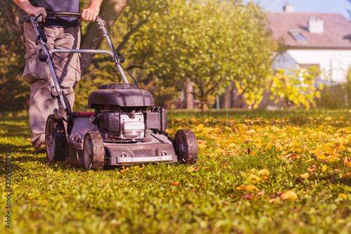 Mowing the grass with a lawn mower in garden at early autumn