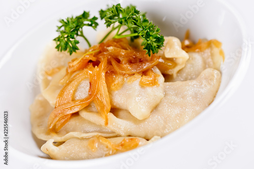 Dumplings filled with potato and topped with fried onion on white plate. Varenyky, vareniki, pierogi, pyrohy