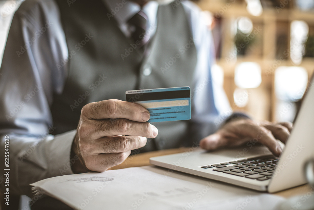 Senior businessman using laptop to check credit card . Focus is on hand. Senior businessman using laptop to check credit card . Focus is on hand.