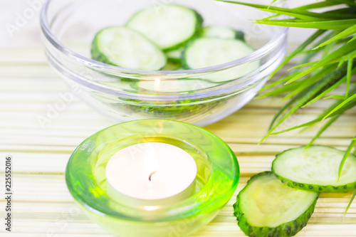 Cucumber home spa and hair care concept. Sliced cucumber, bottles of oil, candle, bathroom towel. Straw light background