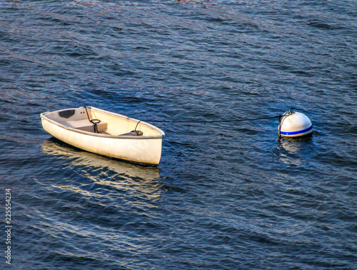Фотография A small white rowboat skiff sits in the water attached by rope to a large round float