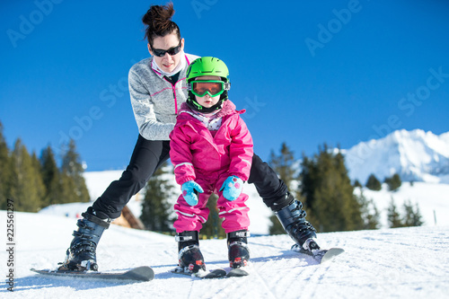 Mother and little child skiing in Alps mountains. Active mom and toddler kid with safety helmet, goggles and poles. Ski lesson for young children. Winter sport for family. Little skier, swiss Alps