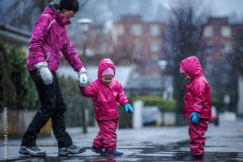 Girls are having fun in water on street in cold autumn day  girls splashing water in rain  happy and cheerful girls enjoying cold weather  kids in pink rain coats and rubber boots