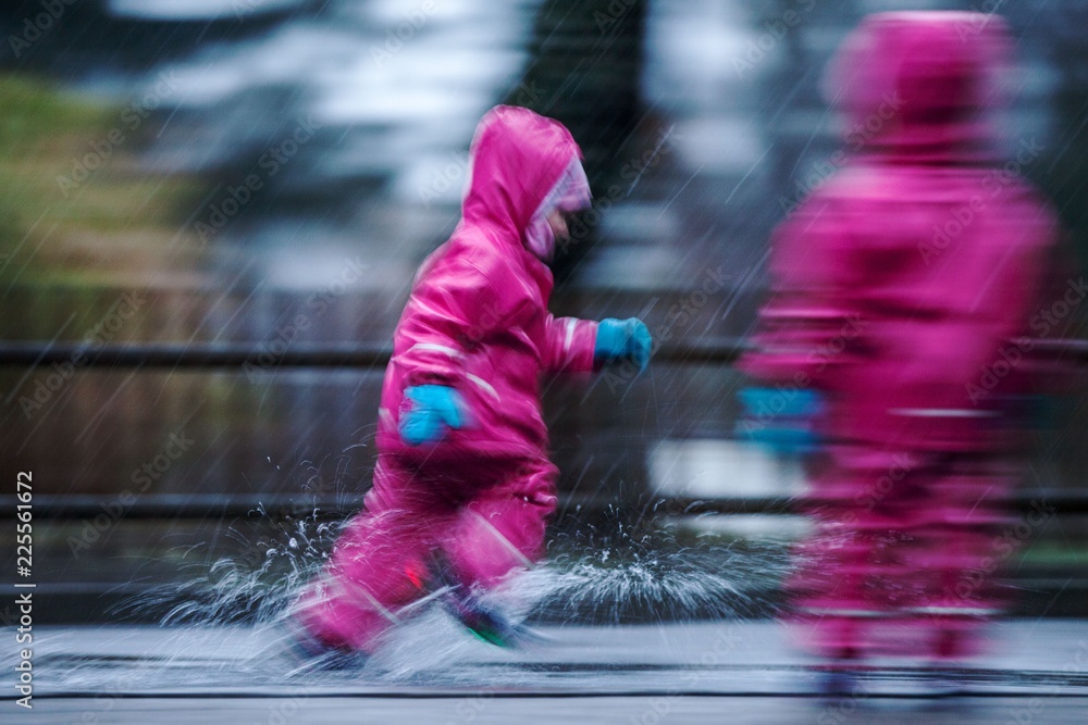 Obraz premium Girls are having fun in water on street in cold autumn day, girls splashing water in rain, happy and cheerful girls enjoying cold weather, kids in pink rain coats and rubber boots