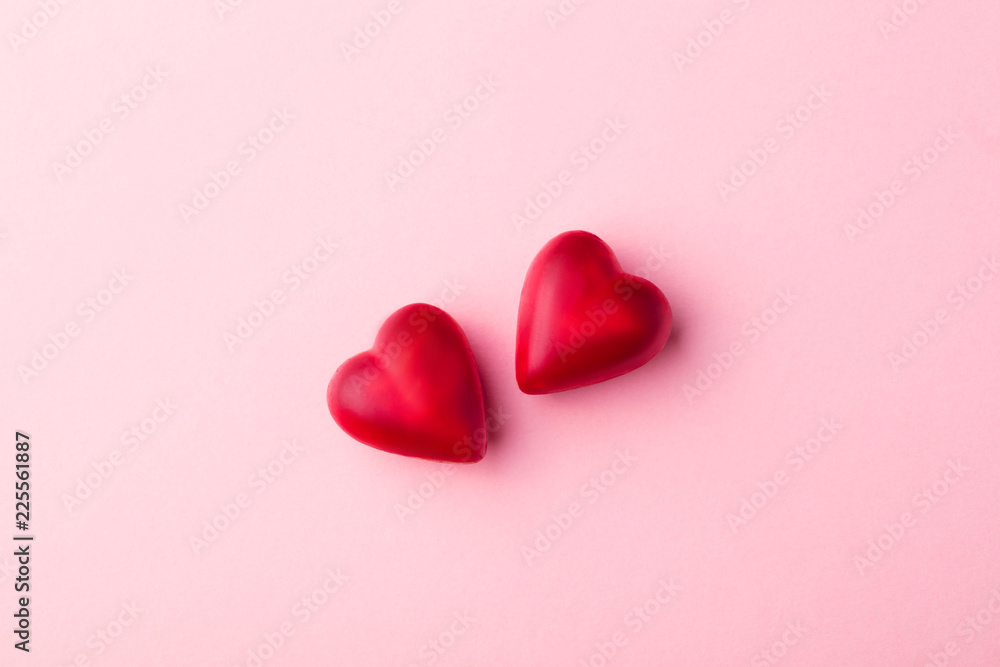 Two chocolate heart candies pink pastel paper background. Top view. Copy space.