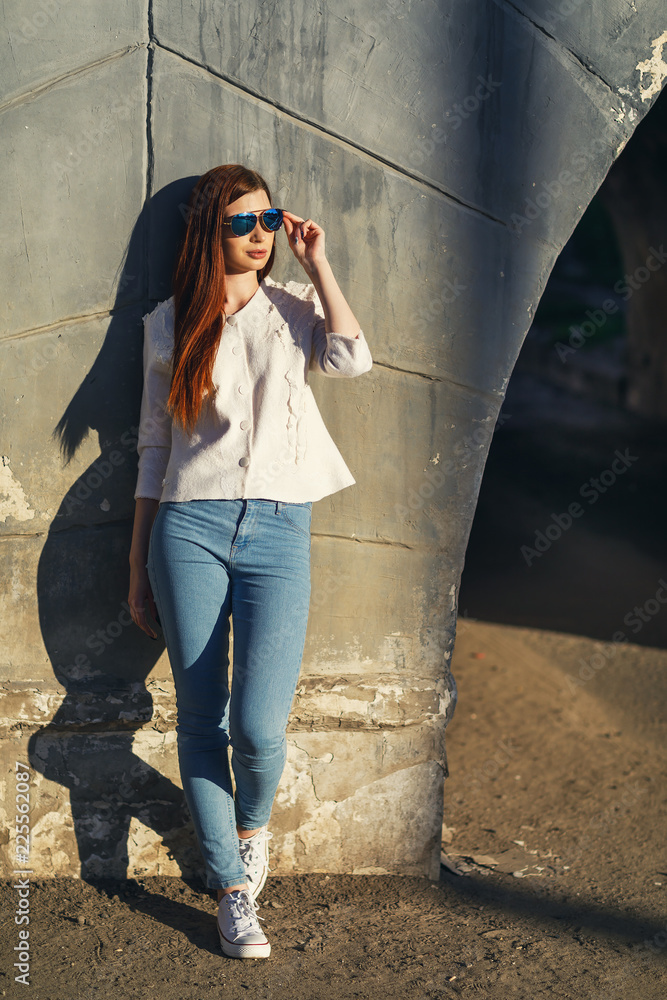 Girl in sunglasses near wall on warm summer evening