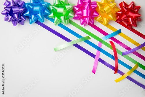 A top view of pink ,yellow, red, green, blue and purple gift wrap bows with diagonally placed ribbons  and ribbon cuts on white background