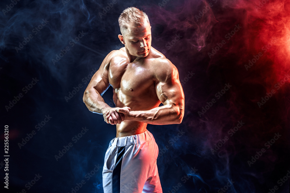 Handsome strong bodybuilder posing in studio on colored smoke background