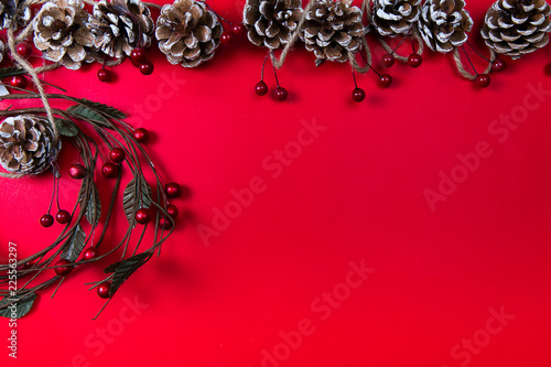 A top view of a christmas ornaments: pine cones and circled twigs with red berries on red background