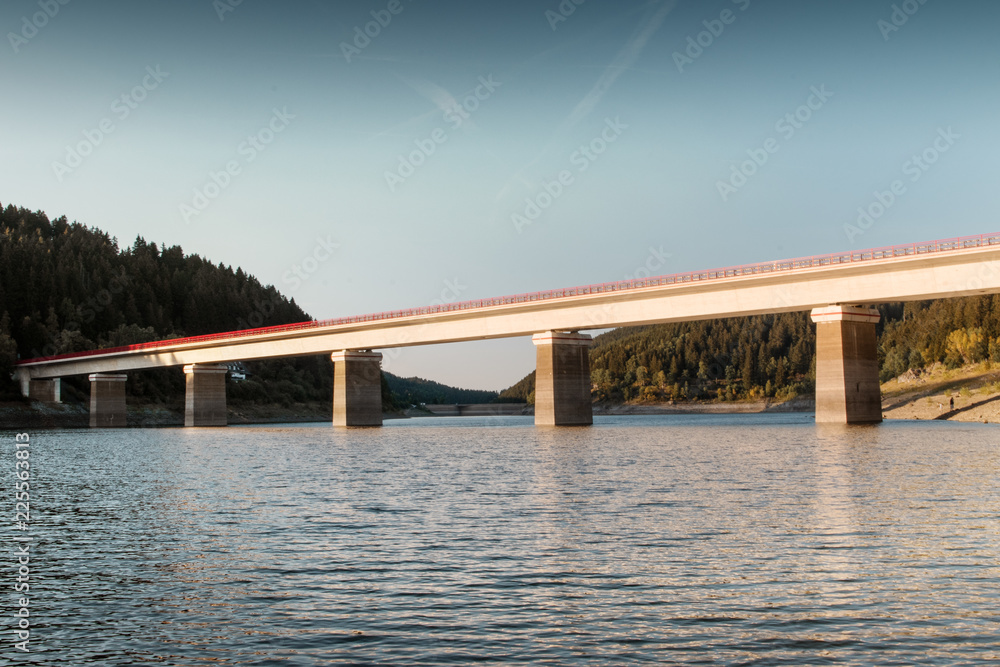 Mountain bridge over a calm beautiful lake with small water ripples and soft evening light in summer sunset. Oker Dam, German Mountains, National park Harz in Germany