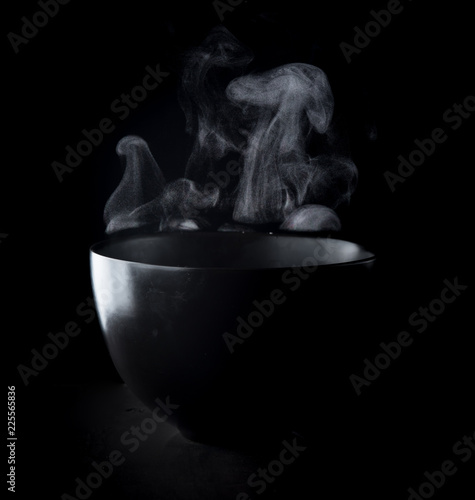 Steam of hot water in a bowl with smoke over dark background