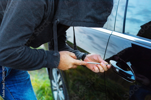 car thief in action, a man in a hood breaks a screwdriver car door