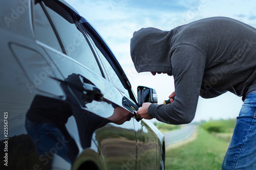 Canvas Print car thief in action, a man in a hood breaks a screwdriver car door