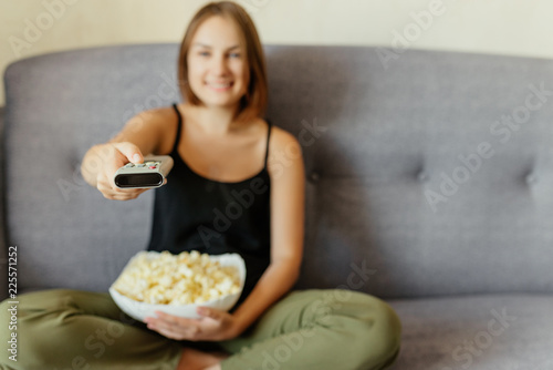 Woman changing channels with a remote control and eating popcorn