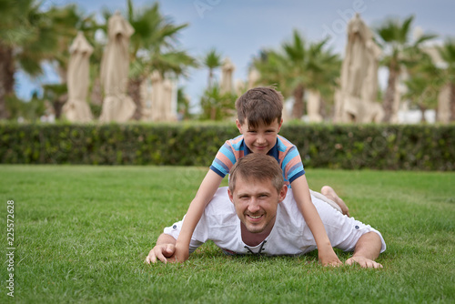 Father and son having fun at the greensward at the hotels territory. They are smiling and looking to the camera.