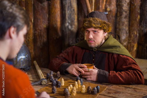 Two men in russian ethnic suit playing medieval popular strategy board game - tafl. Folk, competition and traditional concept