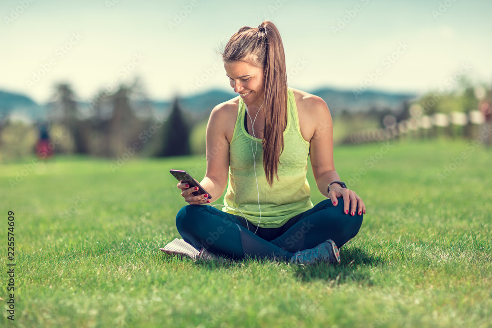 beautiful young sporty brunette relaxing in a park, stretching and looking at her phone beautiful young sporty brunette relaxing in a park, stretching and looking at her phone